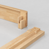 Two light wood pieces with interlocking joinery are positioned on a smooth, light gray surface, showing detailed craftsmanship and precise cuts for assembly.