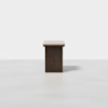 A square table with a light-colored top and a dark rectangular base, placed on a smooth, light gray surface against a plain white background.