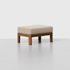 A rectangular ottoman with a light beige upholstered cushion and a wooden frame, set against a plain light gray background.