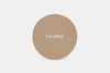 A round, tan felt pad with the word THUMA printed in white capital letters at the center, set against a plain white background.