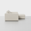 Side view of a modern, light beige sectional sofa with three seat cushions and an attached chaise lounge, set against a plain white background.