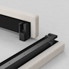 Two sections of a light beige upholstered bed frame are shown on a light surface, with black metal brackets and hardware visible, designed for connecting the two pieces together.