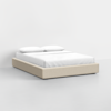 A minimalist bed with a beige upholstered frame, neatly made with white sheets and two white pillows, set against a plain white wall and floor.