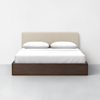 A modern bed with a beige upholstered headboard, two white pillows, white bedding, and a dark brown wooden frame, set against a plain white wall and gray floor.