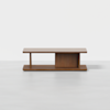 A modern wooden coffee table with a rectangular top, open shelf on one side, and a closed vertical panel in the center, sitting on a light gray surface with a white background.