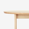 Close-up of the edge and legs of a round, light wood table against a white background.