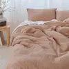 Two neatly arranged pillows with light brown covers and a matching duvet rest on a bed with a white sheet, all against a white textured wall background.