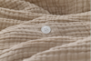 A close-up of a textured beige fabric with horizontal ridges and a single white, four-hole button sewn onto it.