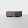 A large, rectangular, brown upholstered ottoman with clean lines sits on a smooth, light-colored floor against a plain white background.