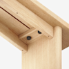 Close-up view of the underside of a light wood table, focusing on the cleanly joined corner with visible screws and smooth, natural wood grain.