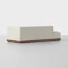 A modern, light beige sectional sofa with clean lines and a low backrest, set on a wooden base, positioned on a smooth, light gray floor against a plain white background.