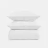 Two white textured pillows stacked on top of a matching white textured comforter, all arranged neatly against a plain, light background.