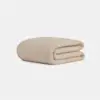A beige, textured blanket neatly folded on a plain white background.