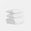 Two white pillows stacked on top of a neatly folded white blanket, all featuring a subtle textured pattern, set against a plain white background.