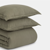 A neatly folded, olive green bedding set with two pillows stacked on top of a matching comforter, all made from a soft, textured fabric, displayed against a plain white background.