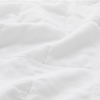 A close-up of a white, soft quilted fabric with subtle stitching and gentle folds, creating a cozy and inviting texture.