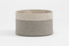 A round, two-toned felt storage basket with light beige on the top half and gray on the bottom half, featuring visible zigzag stitching along the seam, set against a plain white background.
