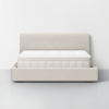 A minimalist beige upholstered bed frame with a white mattress labeled THUMA, set against a plain white wall and a light gray floor.