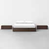 A minimalist bedroom setup featuring a wooden platform bed with white bedding and pillows, flanked by two matching wooden nightstands on each side, all set against a plain white wall and floor.