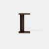 A small, dark brown wooden side table with a modern, minimalist design shaped like an uppercase “I” against a plain light gray background.