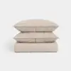 Three beige pillows are stacked neatly on top of a folded beige comforter, placed against a plain white background.