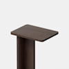 A close-up view of a modern, dark wooden table with a rectangular top and a single thick vertical support, set against a plain light background.