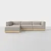 A modern L-shaped sectional sofa with light gray upholstery and a low wooden base, set on a light-colored floor against a plain white background.