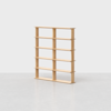 A minimalist wooden bookshelf with five shelves and three vertical dividers, standing empty on a light grey floor against a plain white background.