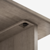 Close-up view of the underside of a wooden table, showing the corner where the tabletop meets the supporting leg and a round plastic adjustable leveling foot embedded in the wood.