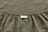 A close-up view of an olive green fitted sheet with an elastic edge and a white care label featuring washing and ironing symbols.