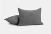 Two dark gray textured pillows, one standing upright and the other lying flat behind it, set against a plain white background.
