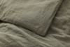 A close-up of a wrinkled olive green bed sheet and matching pillowcase, both made of linen fabric.