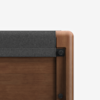Close-up of the corner of a wooden piece of furniture featuring rounded edges and a gray felt covering on top. The image shows smooth brown wood and black circular hardware against a white background.