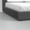 Close-up view of the corner of a bed with a dark gray upholstered frame and white bedding, set on a light gray floor.