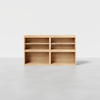 A light wood, rectangular open shelving unit with four compartments, placed on a smooth, light gray floor against a plain white background.
