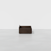 A dark wooden storage box with low sides sits centered on a plain, light gray floor against a white background.