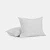 Two light gray square pillows with a simple, minimal design are placed on a plain white background, with one pillow standing upright and the other lying flat behind it.