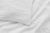 A close-up view of a white pillow and bedsheet with a textured, wavy grid pattern, creating a soft and cozy appearance.