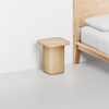 A minimalist wooden nightstand with rounded edges is placed next to a light wood bed with white bedding, set against a white wall and light gray floor.
