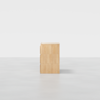 A minimalist three-drawer wooden dresser with a light natural finish, viewed from the side against a plain white background and placed on a smooth gray floor.