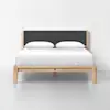 A modern wooden bed frame with a dark gray upholstered headboard, neatly made with white bedding and two pillows, set against a plain white wall and floor.