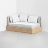 A modern daybed with a light wood frame, beige upholstered backrest, and four white pillows, positioned against a white wall on a gray concrete floor.