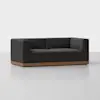 A modern, boxy dark-gray upholstered sofa with deep seats and a low backrest, set on a wooden base, placed on a light gray floor with a plain white background.