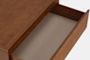 A wooden drawer is pulled open, revealing an empty interior with a light-colored lining. The drawer is part of a wooden piece of furniture, likely a dresser or desk, shown against a plain background.