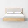 A modern wooden bed with a light wood frame, upholstered headboard, white bedding, and two pillows, placed against a plain white wall on a gray floor.