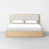 A modern wooden bed with a light wood frame, upholstered headboard, white bedding, and two pillows, placed against a plain white wall on a gray floor.