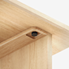 Close-up of a wooden table or furniture joint, showing clean, light wood grain and a recessed hex screw for assembly, highlighting the craftsmanship and secure construction.