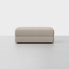 A rectangular, light beige upholstered ottoman with clean lines, set against a plain white background.
