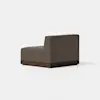 A modern armless brown upholstered chair with a boxy shape and a dark wooden base, shown angled against a plain white background.