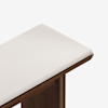 A close-up of a wooden bench with a cushioned seat upholstered in light beige fabric, set against a plain white background.